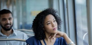 Serious young woman gazes out train car window while using public transportation to reach her destination. Young commuters are riding train.