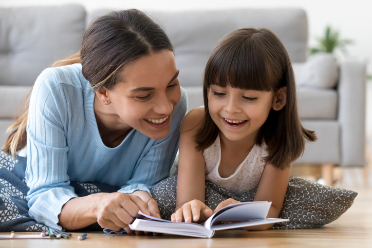 Mother and daughter lying on warm floor reading book