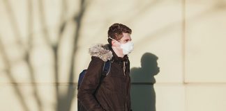 Male student with backpack and mask standing out in the cold.