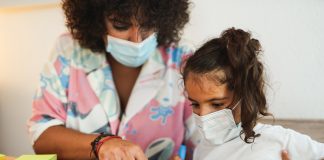 Mother doing home schooling with child while wearing surgical face mask for coronavirus