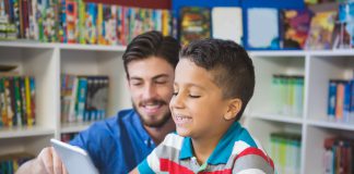 Teacher and school kid using digital table in library at school